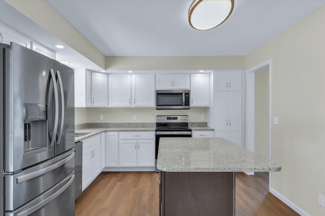 kitchen featuring dark hardwood / wood-style floors, a kitchen island, stainless steel appliances, light stone countertops, and white cabinets