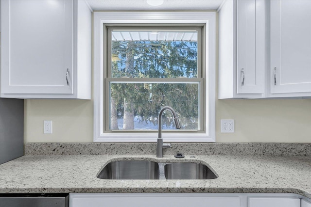 interior details featuring light stone countertops, sink, dishwasher, and white cabinets