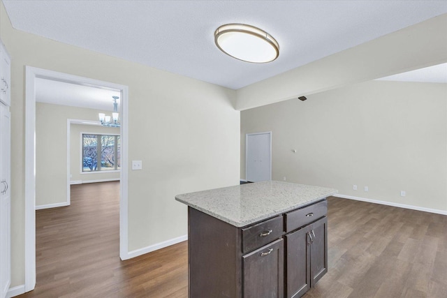 kitchen featuring dark brown cabinets, light stone counters, wood-type flooring, a kitchen island, and a chandelier