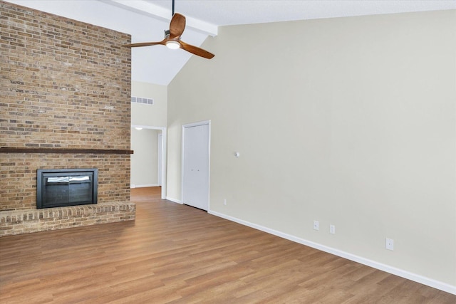 unfurnished living room with ceiling fan, a brick fireplace, light wood-type flooring, and beam ceiling