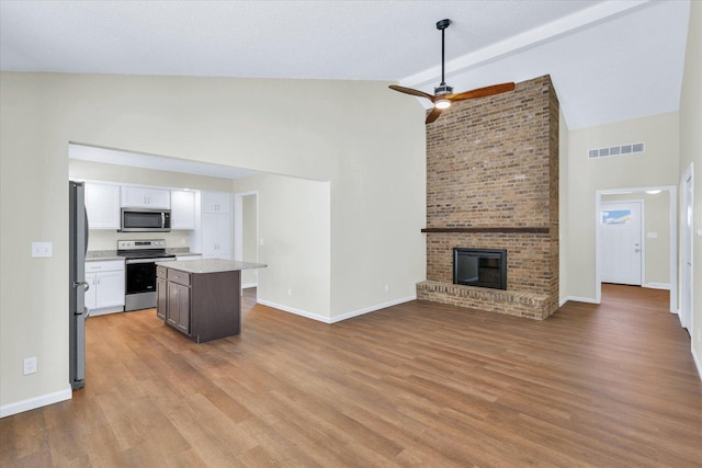 kitchen featuring lofted ceiling, white cabinetry, a kitchen island, stainless steel appliances, and a fireplace