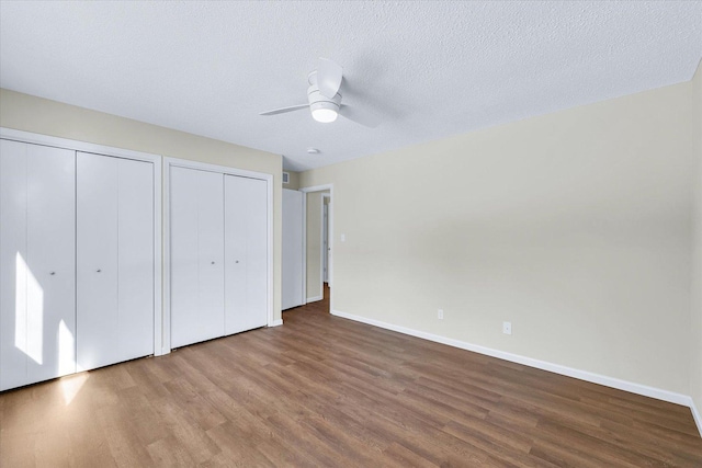 unfurnished bedroom with hardwood / wood-style floors, ceiling fan, two closets, and a textured ceiling