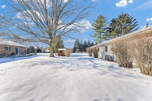 snowy yard featuring cooling unit and a storage shed