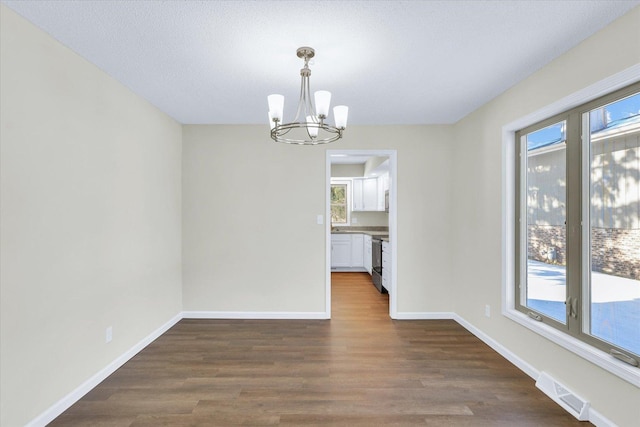 unfurnished dining area with dark hardwood / wood-style flooring, a wealth of natural light, and a chandelier