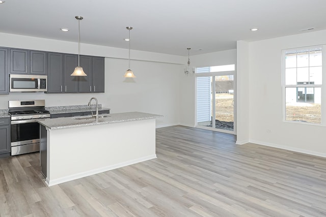 kitchen featuring a kitchen island with sink, hanging light fixtures, sink, light stone countertops, and appliances with stainless steel finishes