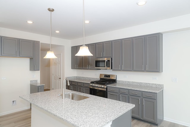 kitchen featuring gray cabinetry, sink, stainless steel appliances, an island with sink, and decorative light fixtures