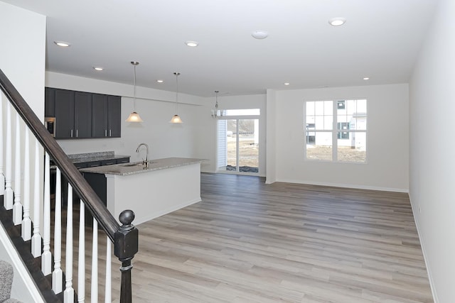 kitchen featuring light stone countertops, pendant lighting, light hardwood / wood-style flooring, and sink