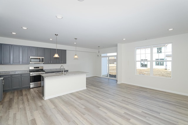 kitchen with sink, light stone countertops, an island with sink, decorative light fixtures, and stainless steel appliances