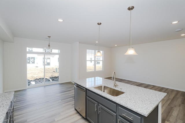 kitchen with stainless steel dishwasher, sink, decorative light fixtures, light hardwood / wood-style floors, and an island with sink