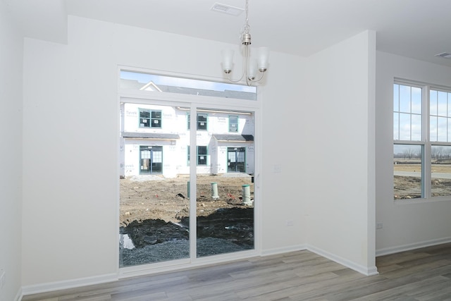 unfurnished dining area with wood-type flooring and a notable chandelier