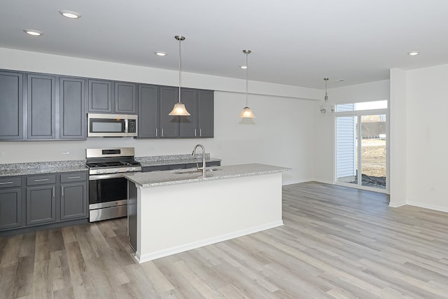 kitchen featuring stainless steel appliances, a kitchen island with sink, sink, gray cabinets, and hanging light fixtures