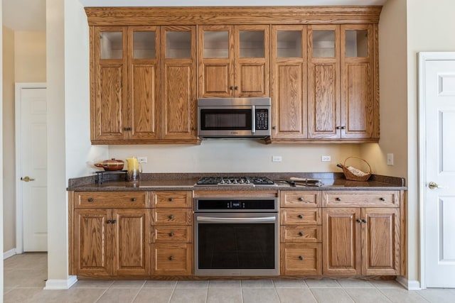 kitchen with light tile patterned floors, appliances with stainless steel finishes, and dark stone countertops