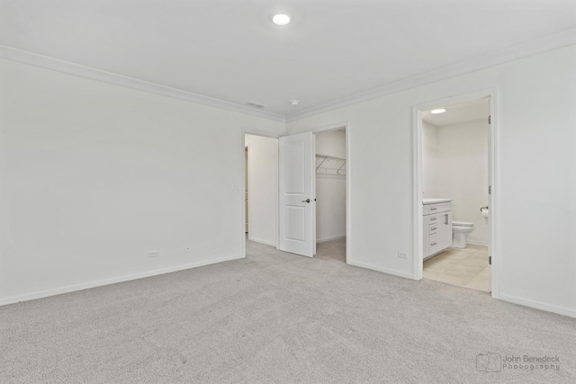 unfurnished bedroom with a closet, a spacious closet, ornamental molding, and ensuite bath