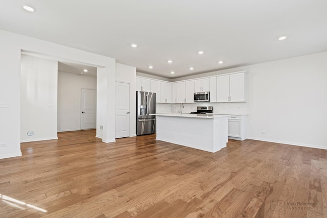 kitchen featuring a kitchen island with sink, light hardwood / wood-style flooring, decorative backsplash, white cabinets, and appliances with stainless steel finishes