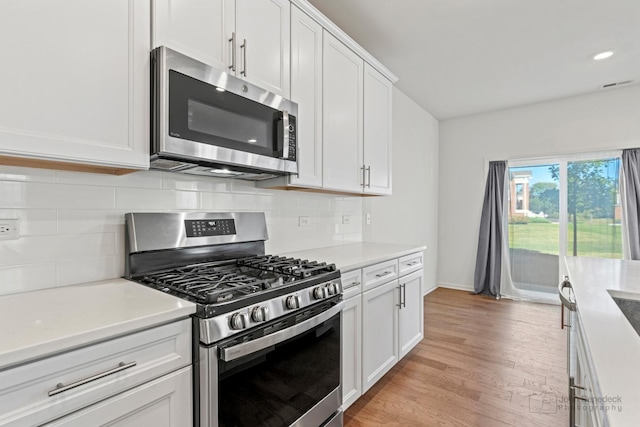 kitchen featuring backsplash, white cabinets, stainless steel appliances, and light hardwood / wood-style floors