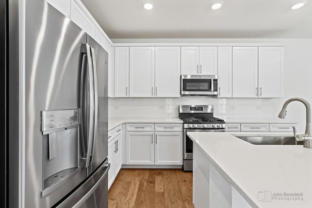 kitchen featuring sink, light wood-type flooring, tasteful backsplash, white cabinetry, and stainless steel appliances