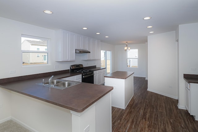 kitchen with dark wood-type flooring, kitchen peninsula, sink, stainless steel gas range, and white cabinetry