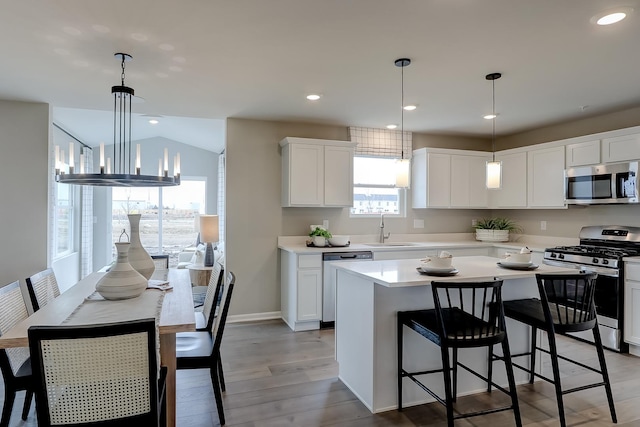 kitchen with appliances with stainless steel finishes, sink, decorative light fixtures, white cabinetry, and a kitchen island