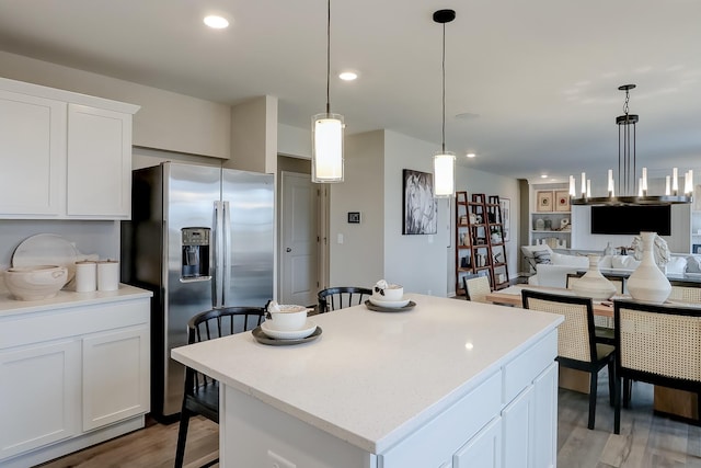 kitchen with stainless steel refrigerator with ice dispenser, light wood-type flooring, decorative light fixtures, a center island, and white cabinetry