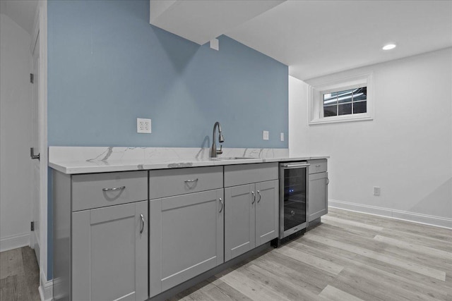 kitchen featuring light stone countertops, wine cooler, sink, gray cabinets, and light wood-type flooring