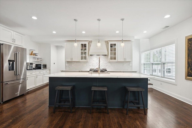 kitchen featuring a center island with sink, stainless steel appliances, dark wood-type flooring, custom range hood, and pendant lighting