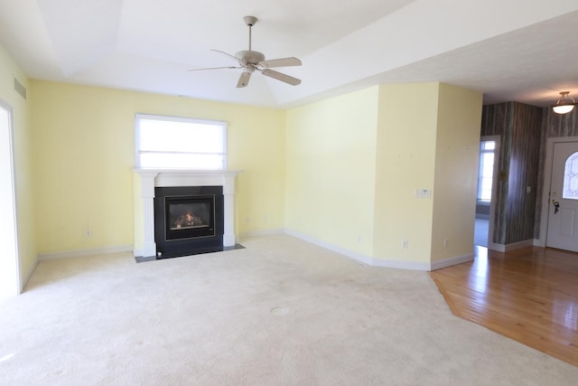 unfurnished living room featuring a healthy amount of sunlight, ceiling fan, light colored carpet, and a tray ceiling