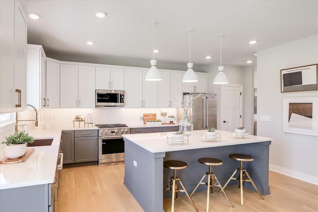 kitchen featuring high end appliances, pendant lighting, light hardwood / wood-style flooring, a center island, and a breakfast bar area