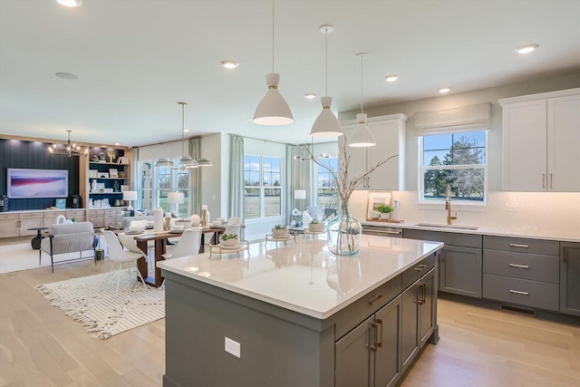 kitchen with sink, pendant lighting, white cabinets, a center island, and light hardwood / wood-style floors