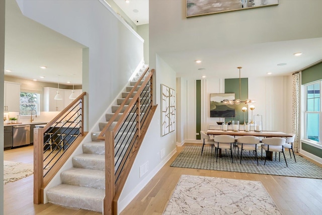 stairs with hardwood / wood-style floors, a healthy amount of sunlight, and a notable chandelier