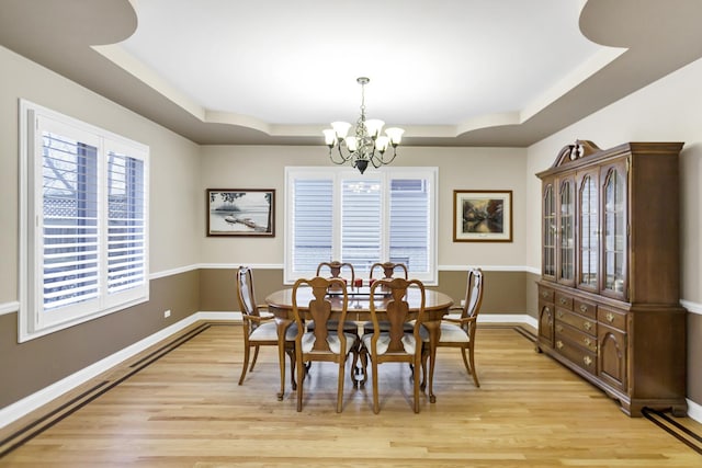 dining space with a notable chandelier, a tray ceiling, and light hardwood / wood-style floors