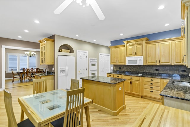 kitchen featuring light hardwood / wood-style floors, a center island, white appliances, dark stone counters, and ceiling fan with notable chandelier