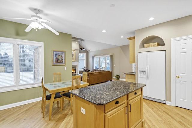 kitchen with dark stone countertops, a center island, a healthy amount of sunlight, light wood-type flooring, and white refrigerator with ice dispenser