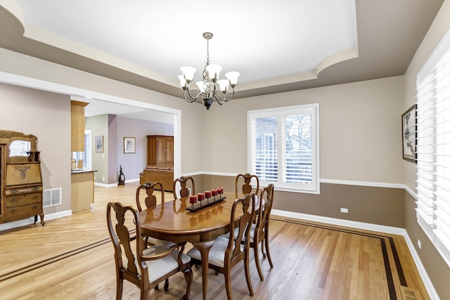 dining space with a tray ceiling, light hardwood / wood-style flooring, and a chandelier