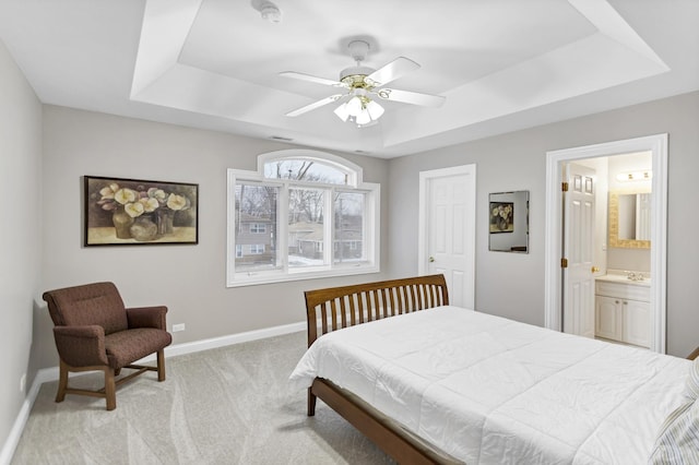 carpeted bedroom featuring a raised ceiling, ceiling fan, sink, and ensuite bathroom