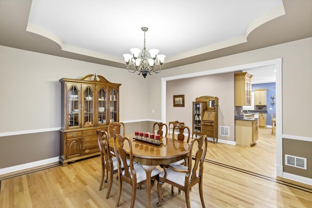 dining room featuring light hardwood / wood-style floors, a raised ceiling, and a notable chandelier