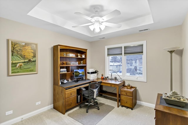 carpeted office featuring a raised ceiling and ceiling fan