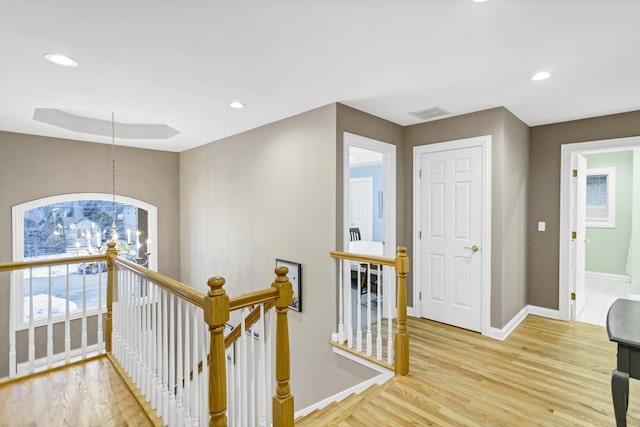 hallway featuring light wood-type flooring, a raised ceiling, and a notable chandelier