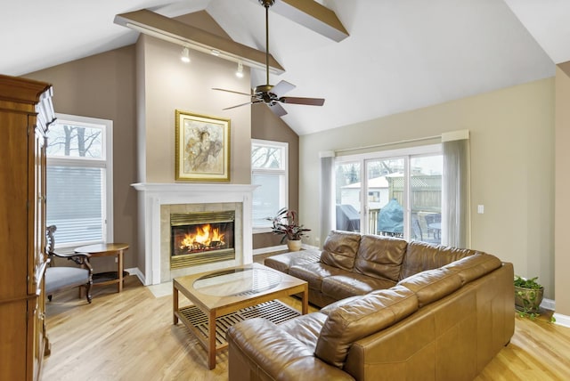 living room with ceiling fan, lofted ceiling with beams, a tiled fireplace, and light hardwood / wood-style flooring