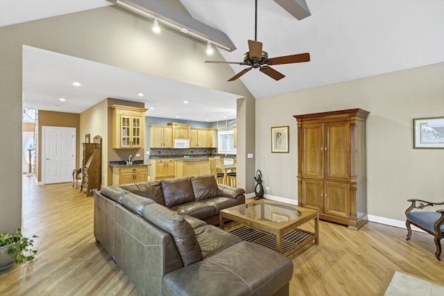 living room with ceiling fan, vaulted ceiling, track lighting, and light hardwood / wood-style flooring