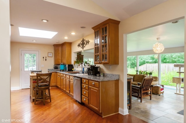 kitchen with light stone countertops, vaulted ceiling with skylight, sink, light hardwood / wood-style flooring, and dishwasher