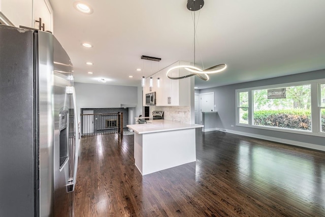 kitchen with backsplash, white cabinets, hanging light fixtures, kitchen peninsula, and stainless steel appliances