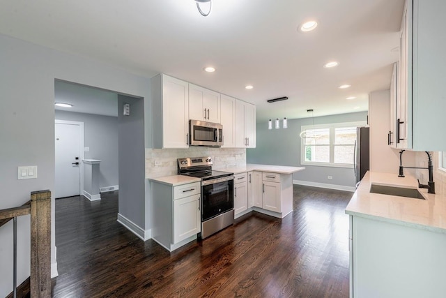 kitchen with sink, stainless steel appliances, kitchen peninsula, decorative light fixtures, and white cabinets