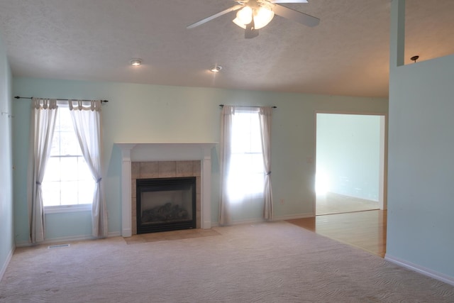 unfurnished living room with a tiled fireplace, light colored carpet, a textured ceiling, and ceiling fan