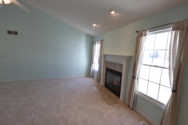 unfurnished living room featuring a healthy amount of sunlight, a tiled fireplace, vaulted ceiling, and light carpet