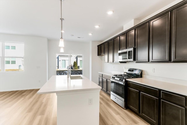 kitchen featuring appliances with stainless steel finishes, sink, hanging light fixtures, dark brown cabinetry, and a center island with sink