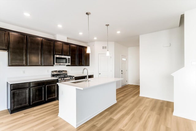 kitchen with sink, dark brown cabinets, hanging light fixtures, stainless steel appliances, and a kitchen island with sink