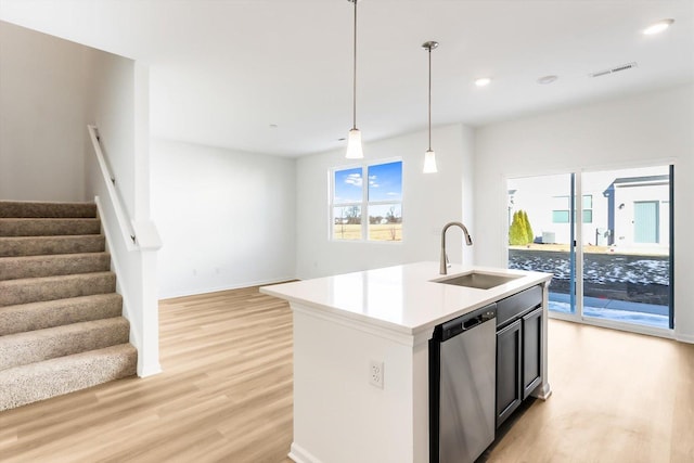 kitchen with decorative light fixtures, sink, stainless steel dishwasher, light hardwood / wood-style floors, and a center island with sink