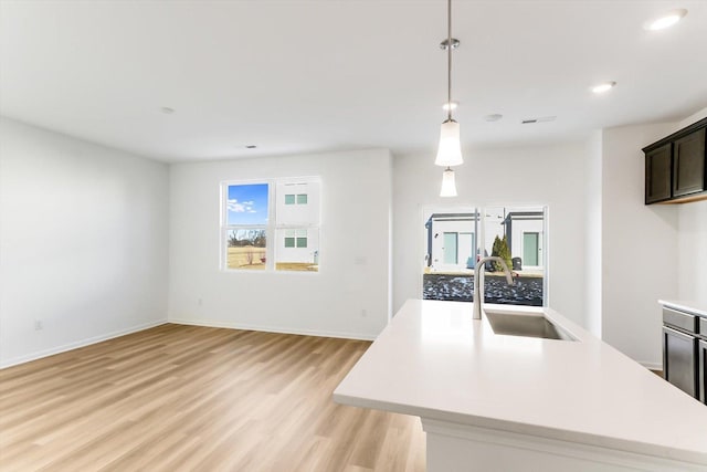 kitchen featuring hanging light fixtures, sink, a center island with sink, and light hardwood / wood-style flooring