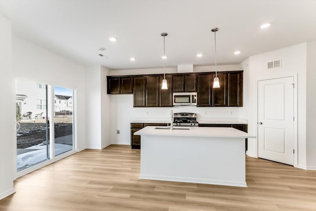 kitchen featuring appliances with stainless steel finishes, a center island with sink, light hardwood / wood-style floors, and decorative light fixtures