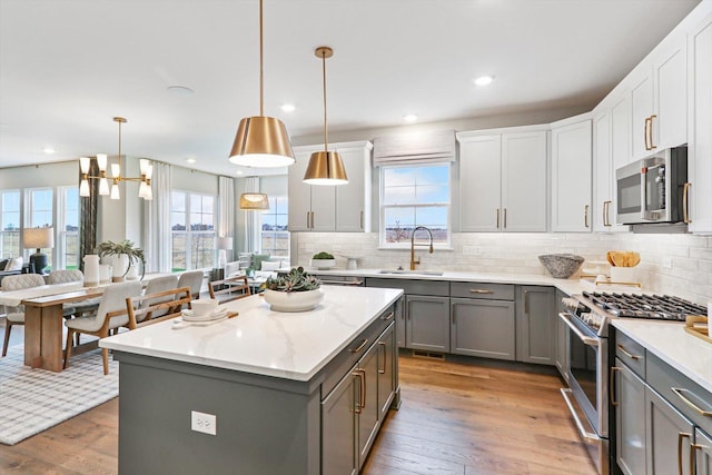 kitchen with gray cabinetry, light wood-type flooring, decorative light fixtures, a kitchen island, and stainless steel appliances